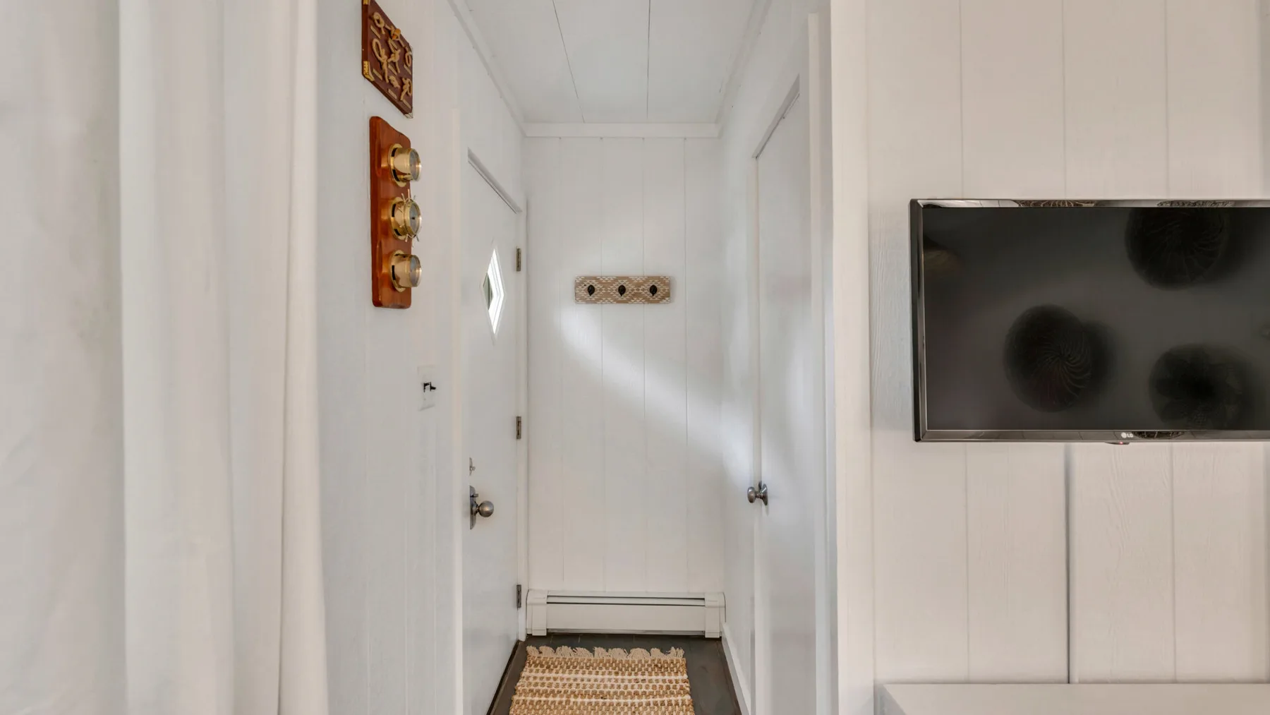 A narrow white hallway with a closed door and a wall-mounted television.