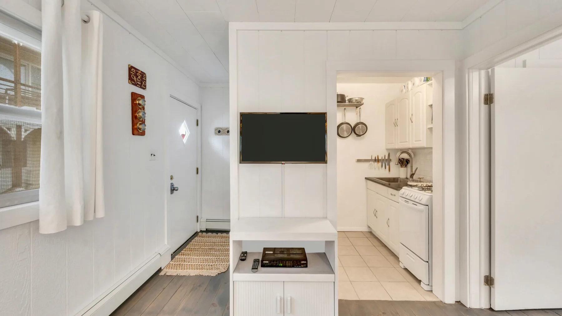 A bright interior shows a small kitchen beside a television and window.