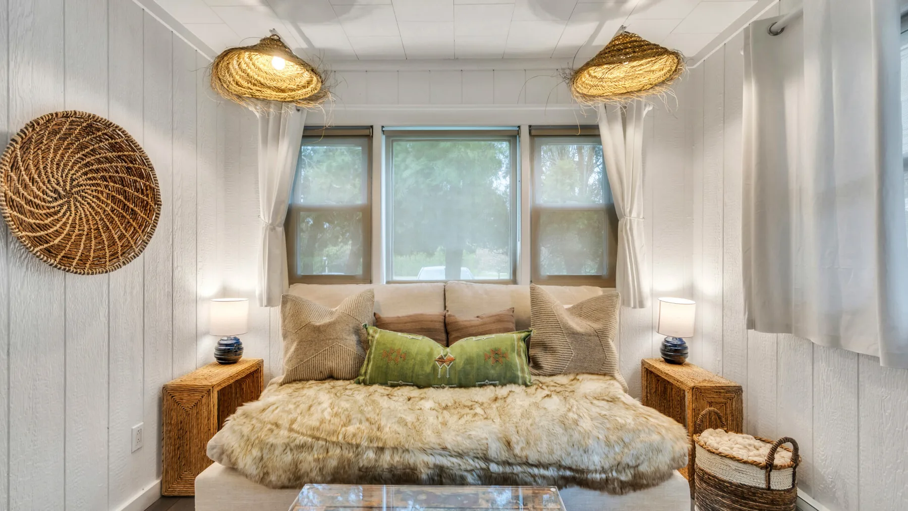 A bedroom with a bed beneath three windows and woven pendant lights.