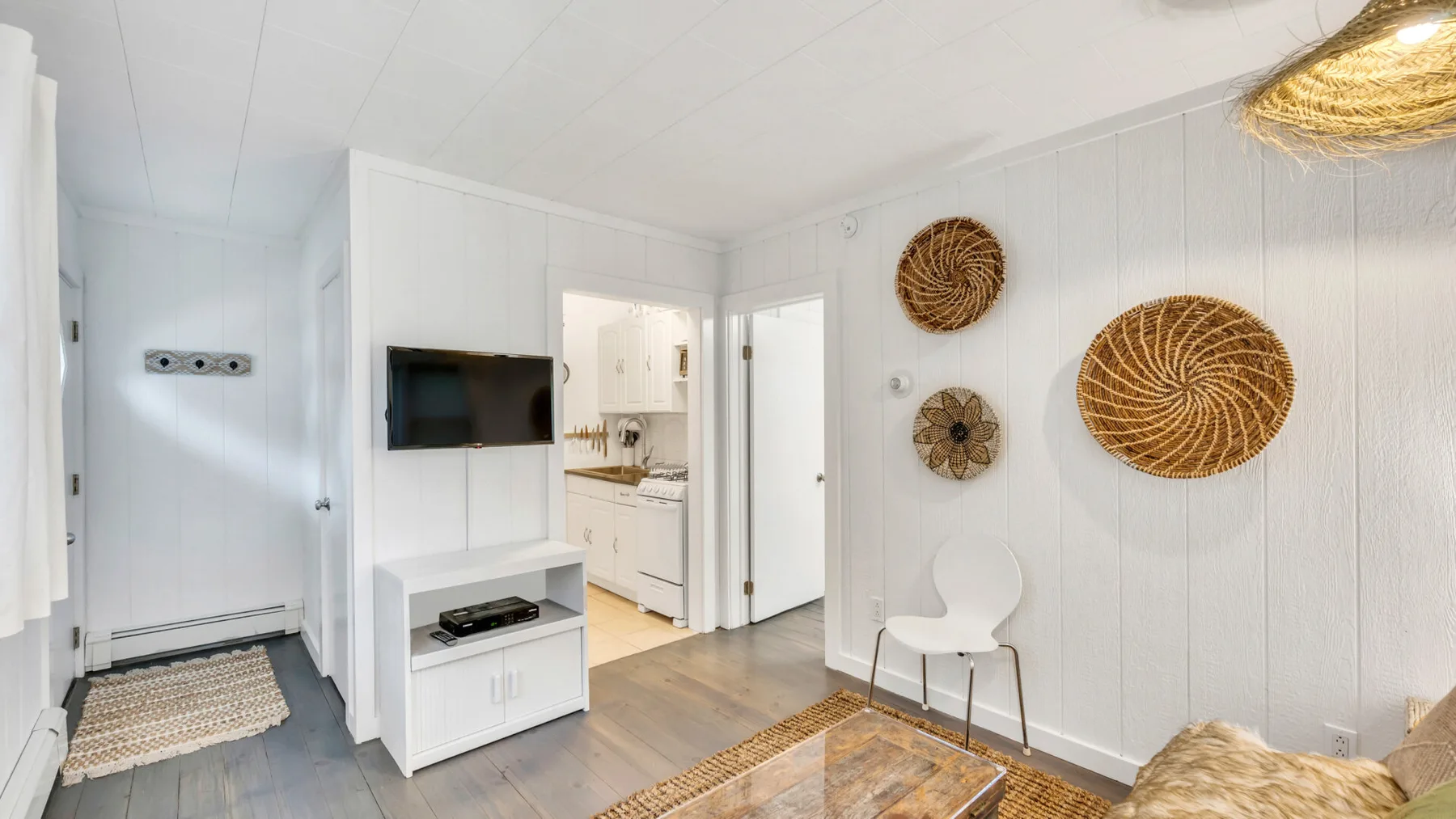 A bright living area with a wall-mounted television and decorative woven wall pieces.