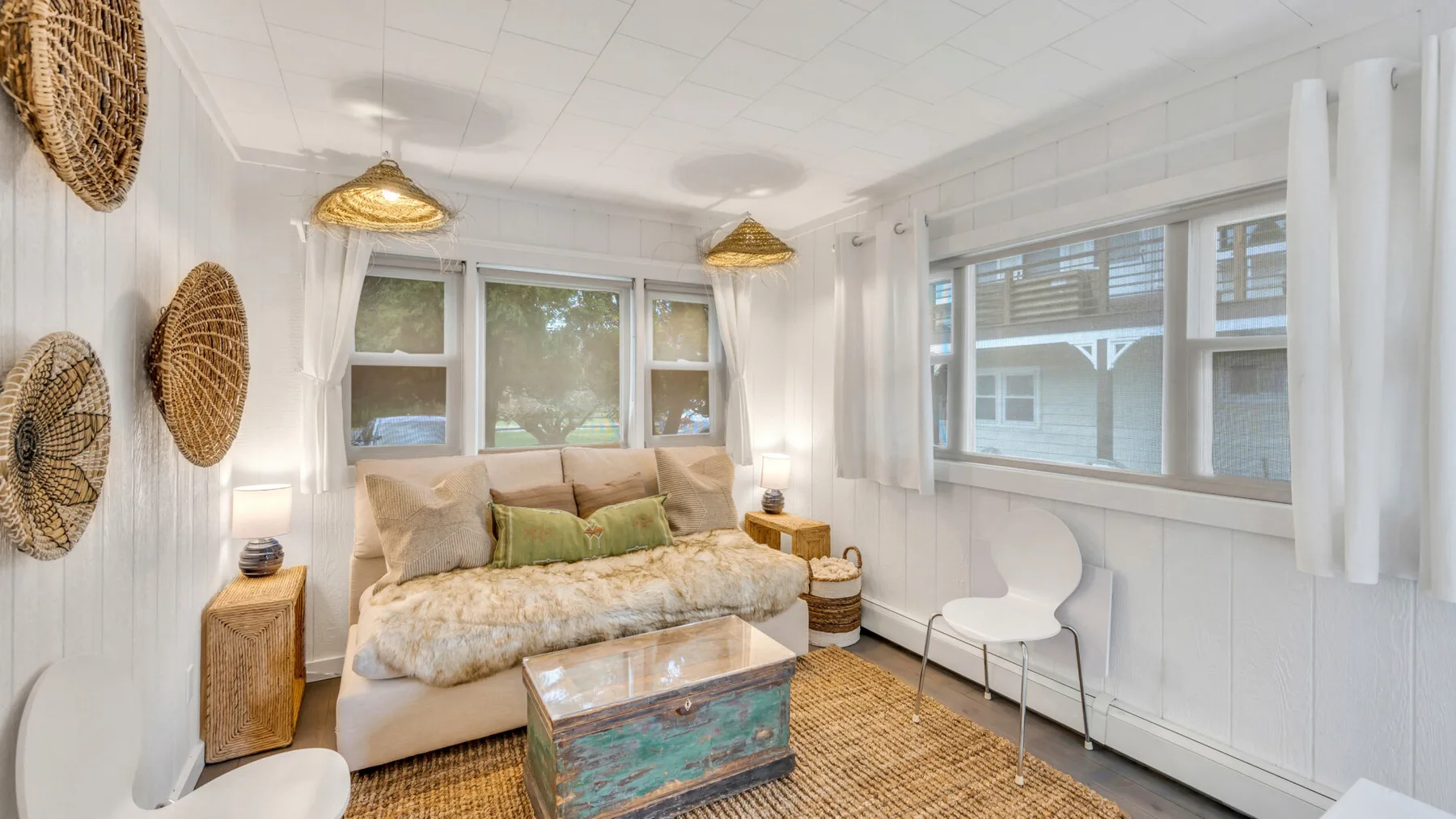 A bright sitting room has a sofa, a small table, and woven wall decorations.