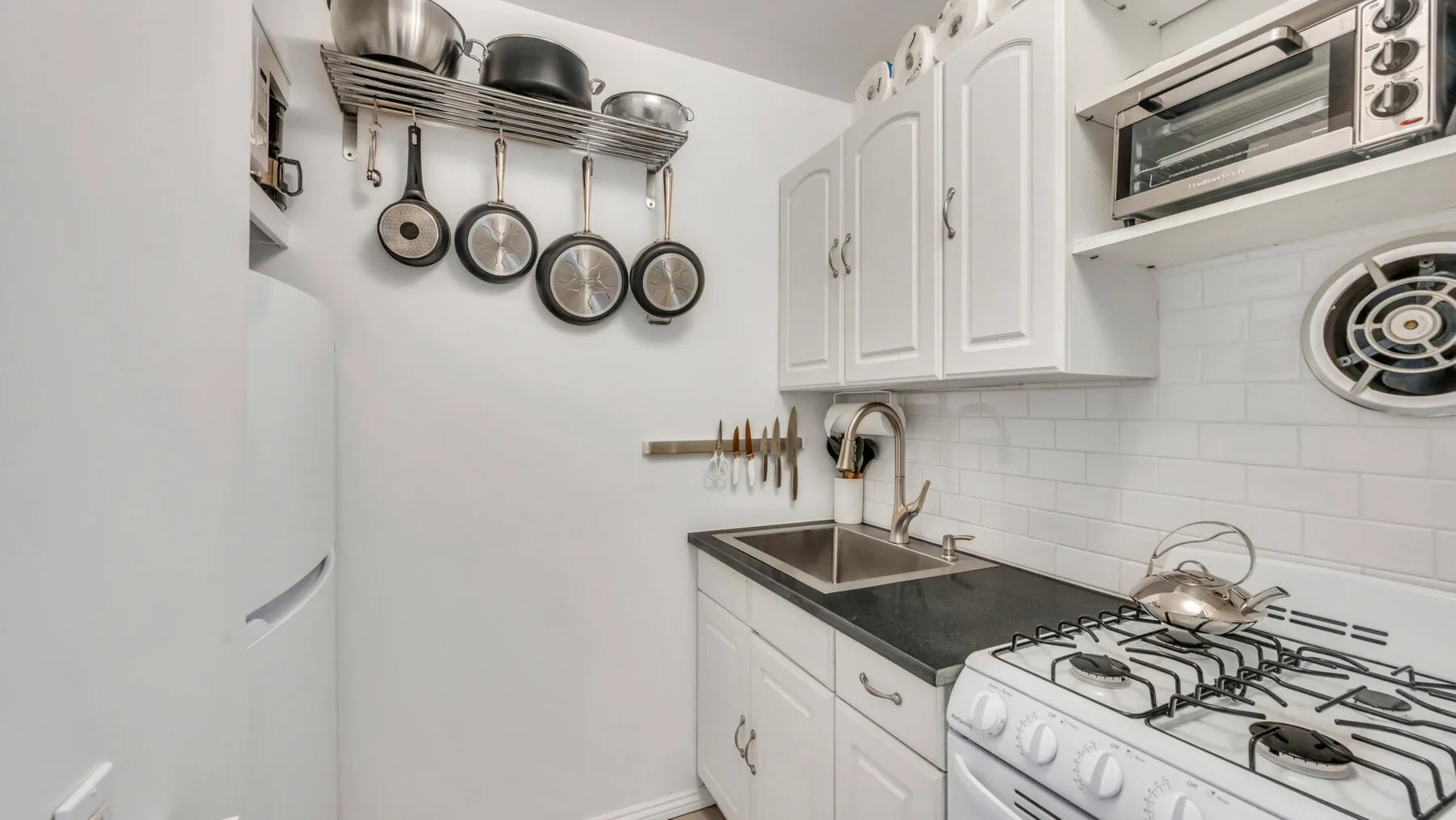 A compact kitchen with white cabinets, dark counters, and cooking appliances.