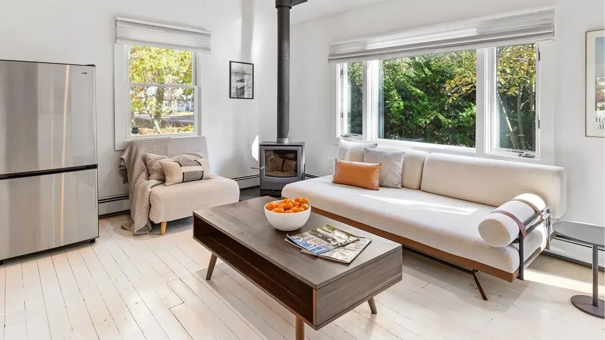 A bright living room with a long sofa and large windows overlooking greenery.