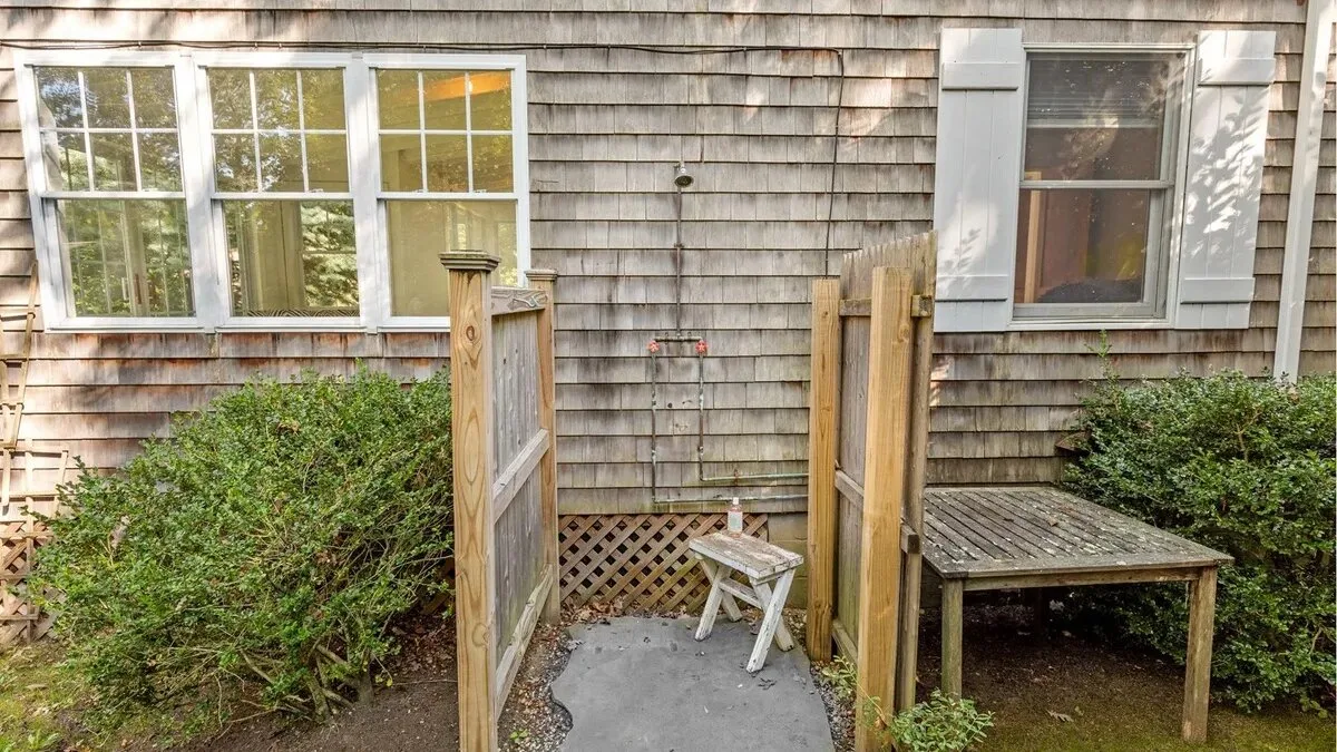 A small outdoor patio with a wooden table and white folding stool.