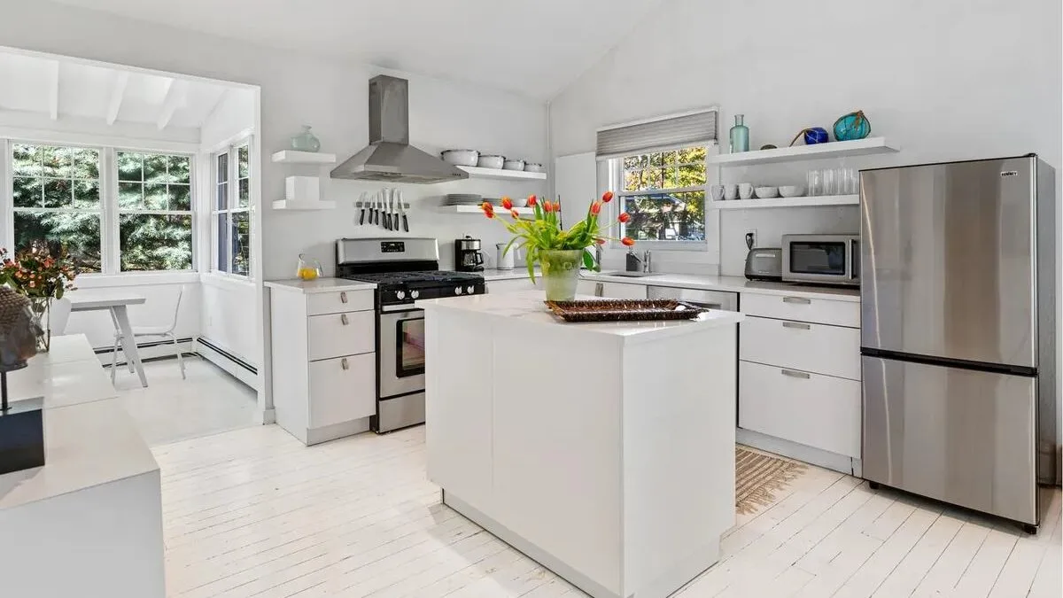 A bright white kitchen with a central island and stainless steel appliances.