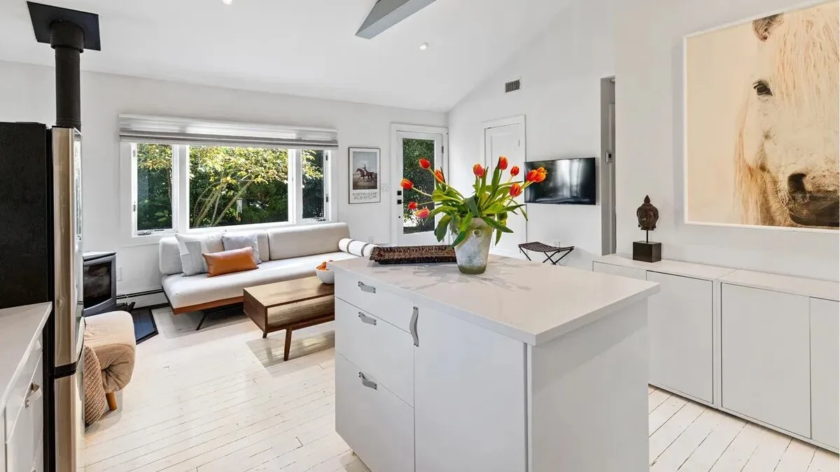A bright open-plan living room and kitchen with a white island and large windows.