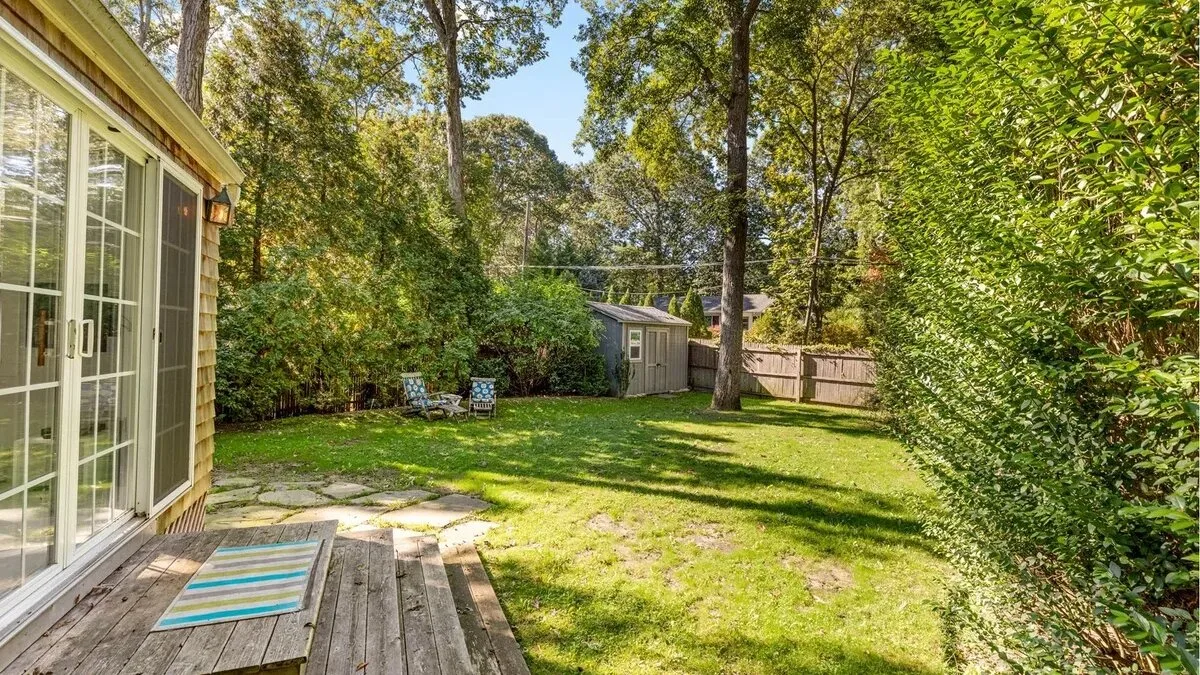 A backyard patio overlooks a grassy yard bordered by trees and shrubs.