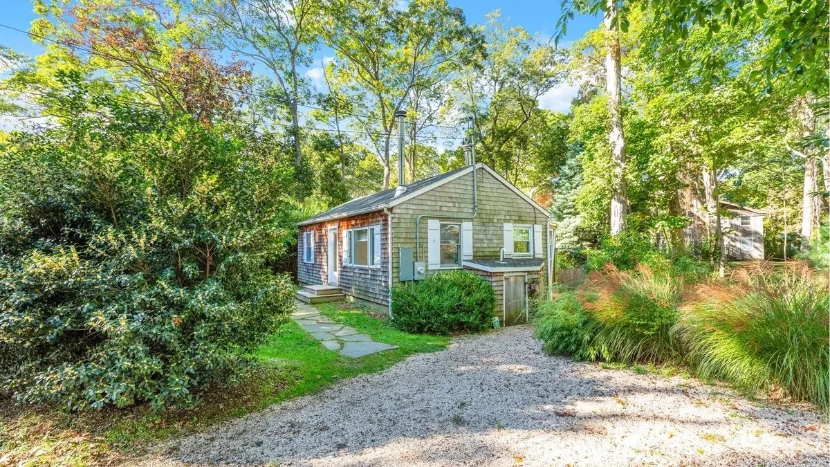 A small house sits among trees beside a gravel driveway.