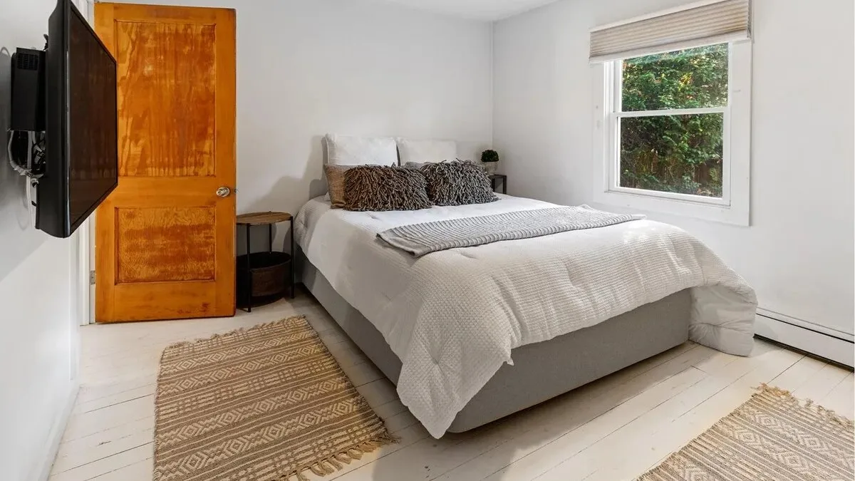 A bright bedroom with a neatly made bed and a window overlooking greenery.