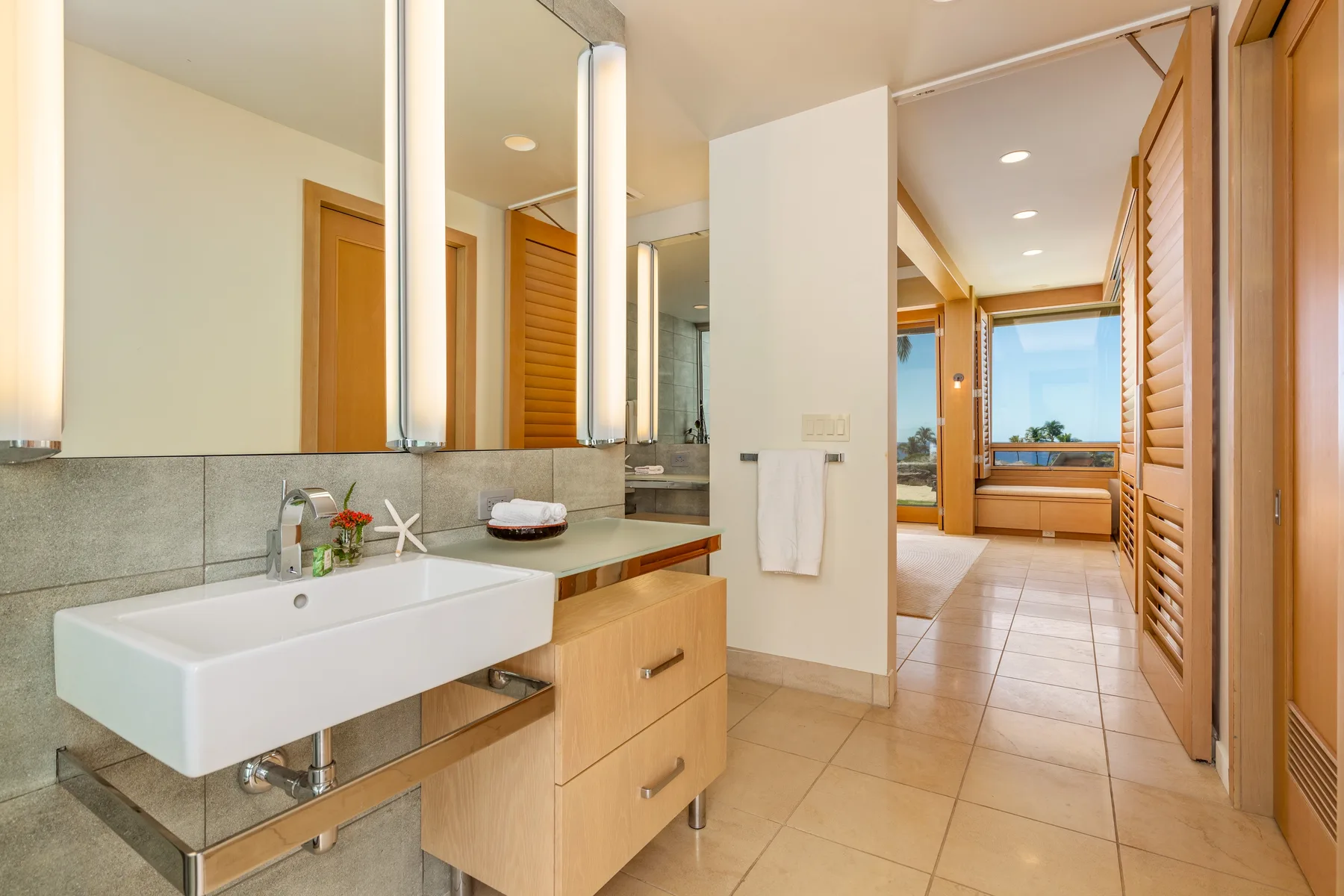 Baño luminoso con lavabo suspendido, armarios con espejo y una ventana al fondo.