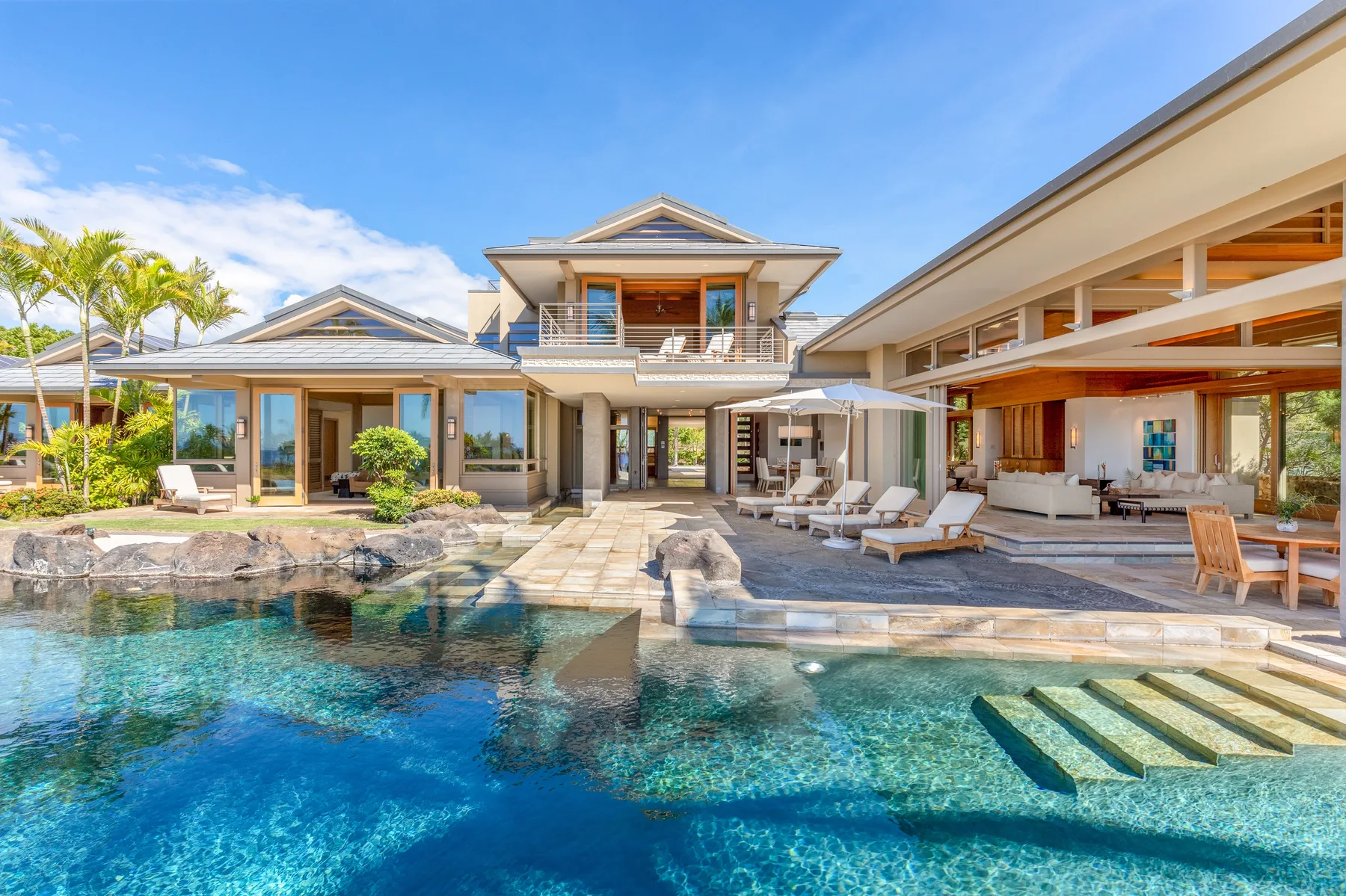 A modern villa surrounds a swimming pool, with a patio and outdoor seating.