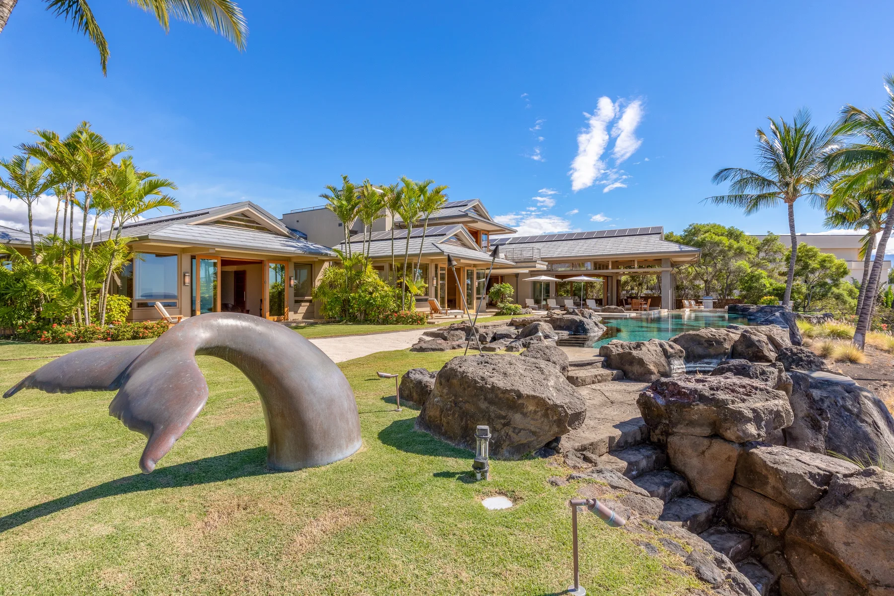 Un edificio de estilo tropical da a una piscina ajardinada con rocas y palmeras.