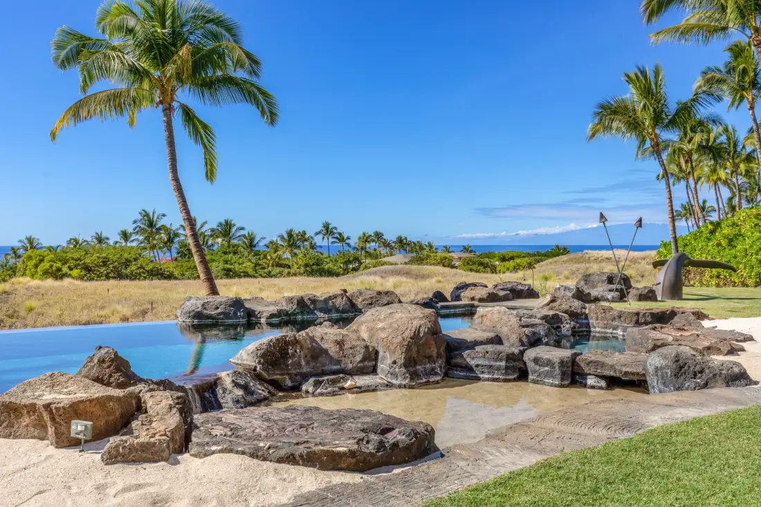 Una piscina tropical al aire libre con rocas y palmeras junto al océano.