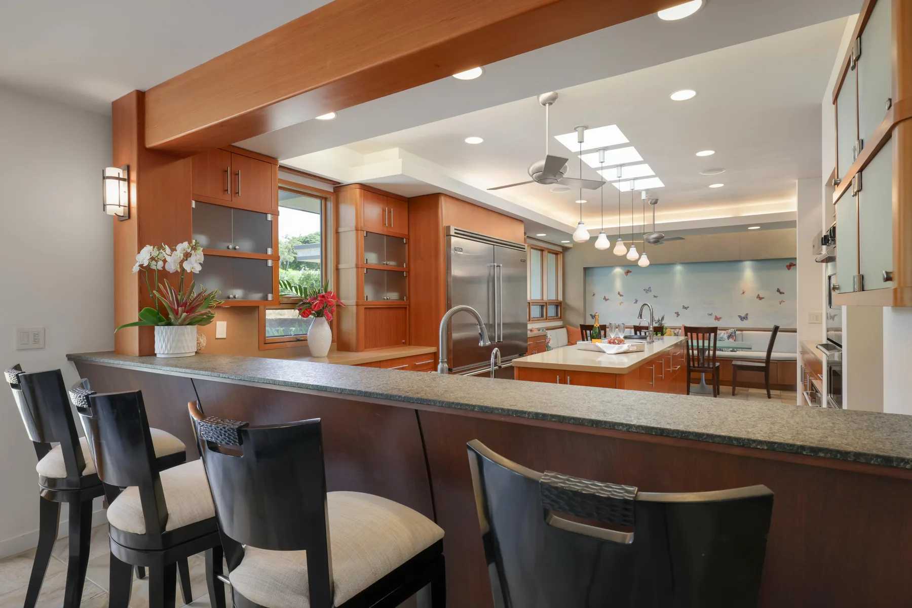 Una cocina abierta con comedor tiene una barra larga con asientos y luces colgantes.