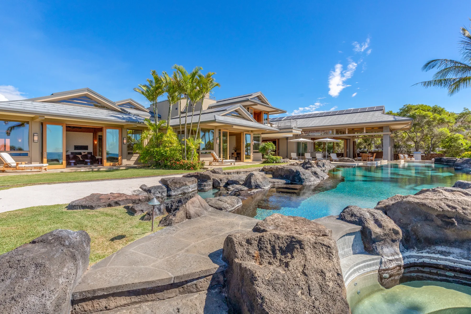 Una casa moderna se abre a una piscina ajardinada con grandes rocas junto al agua.