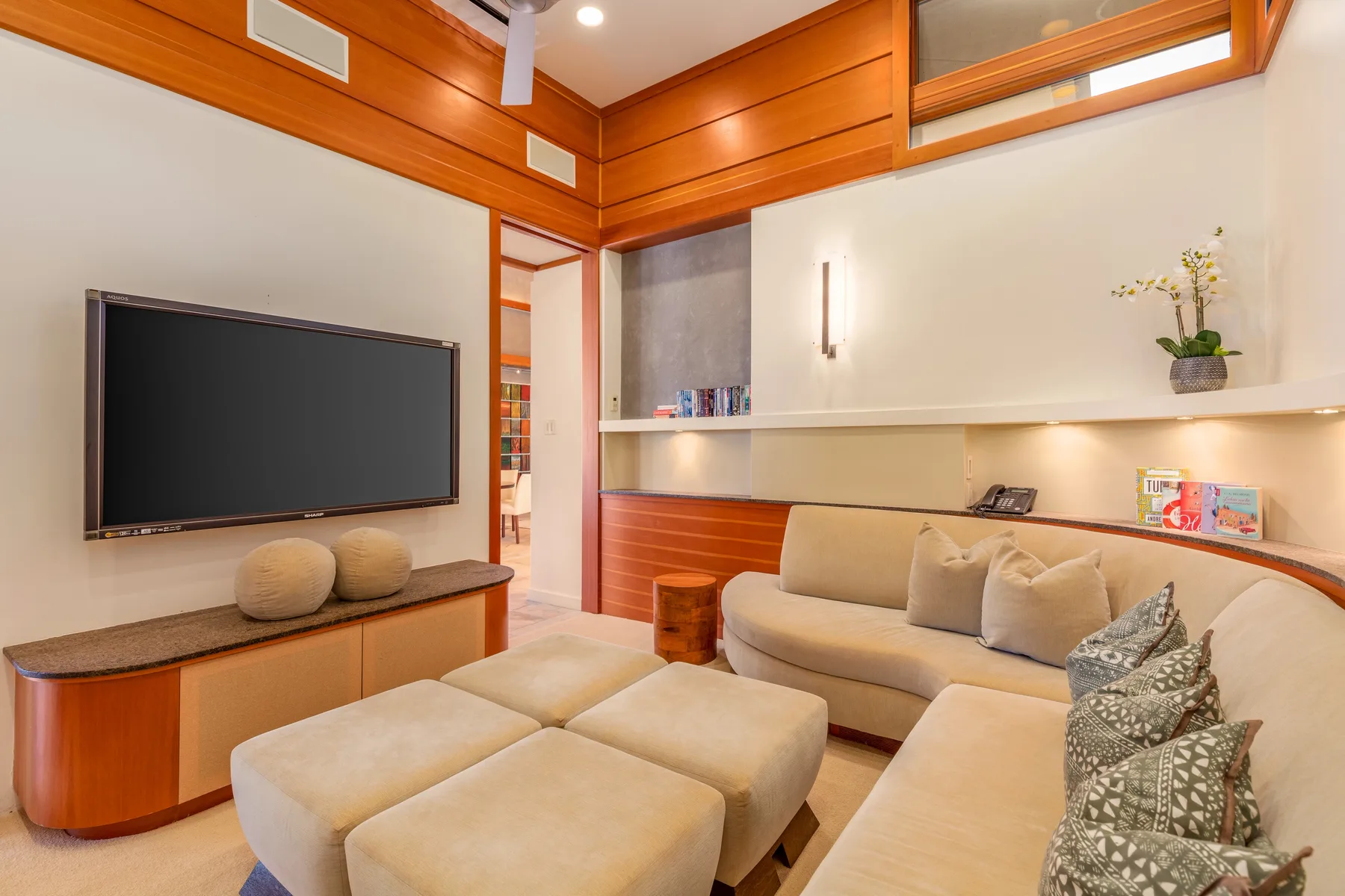A living room with a wall-mounted television and light-colored seating.