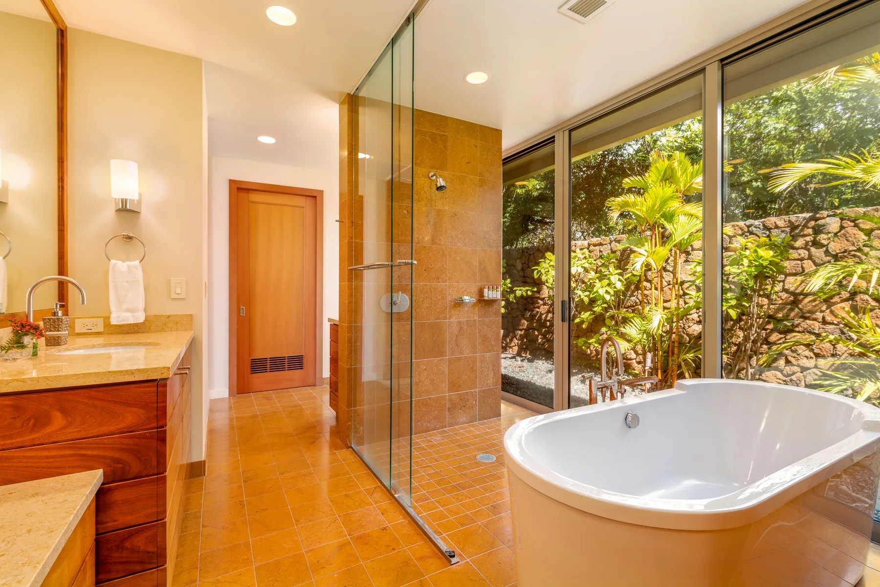 Un baño con bañera, zona de ducha acristalada y grandes ventanas con vistas a la vegetación.