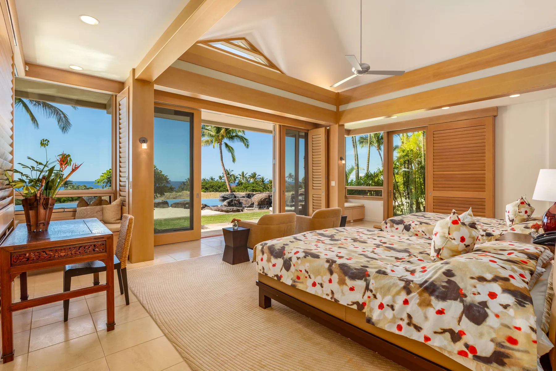 Un dormitorio con una colcha floral y grandes ventanas con vistas a las palmeras.