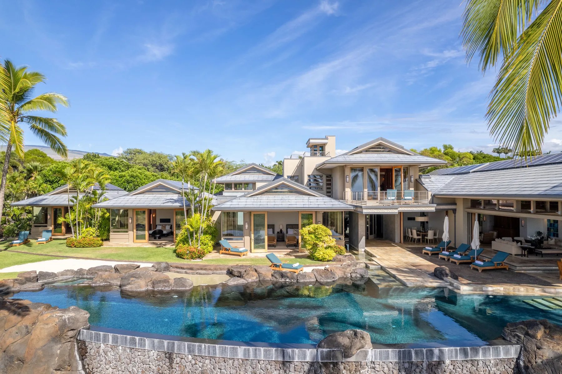 Una gran villa tropical da a una piscina rodeada de rocas y palmeras.