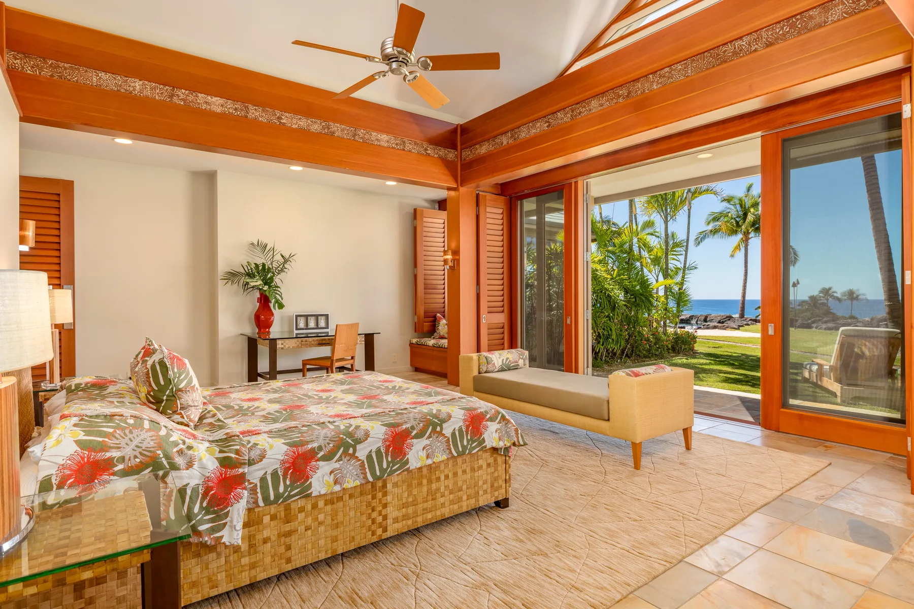 Un dormitorio tropical con una colcha floral y amplias puertas corredizas de vidrio.