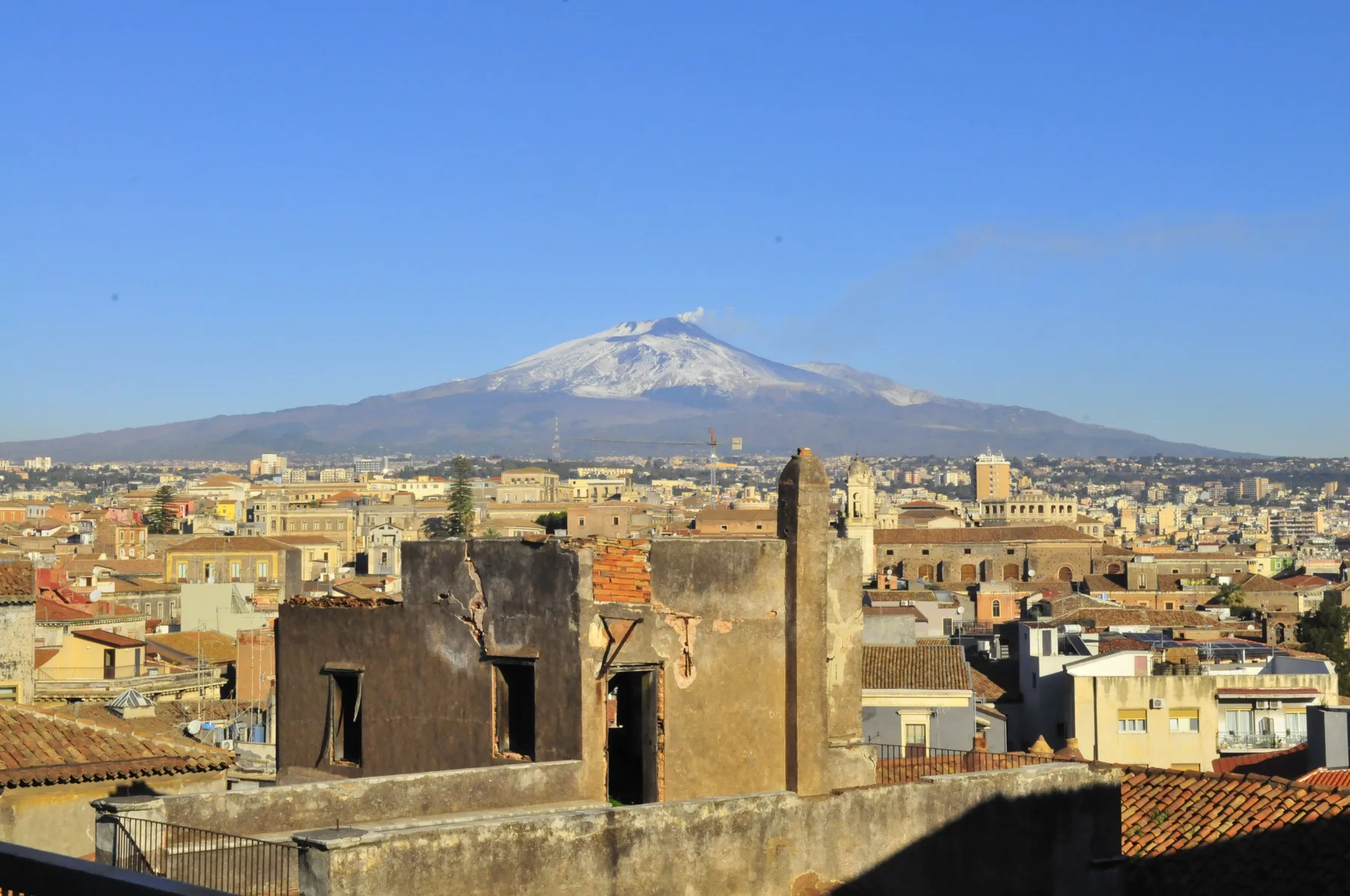 A cityscape spreads across the foreground beneath a snow-capped mountain and clear blue sky.