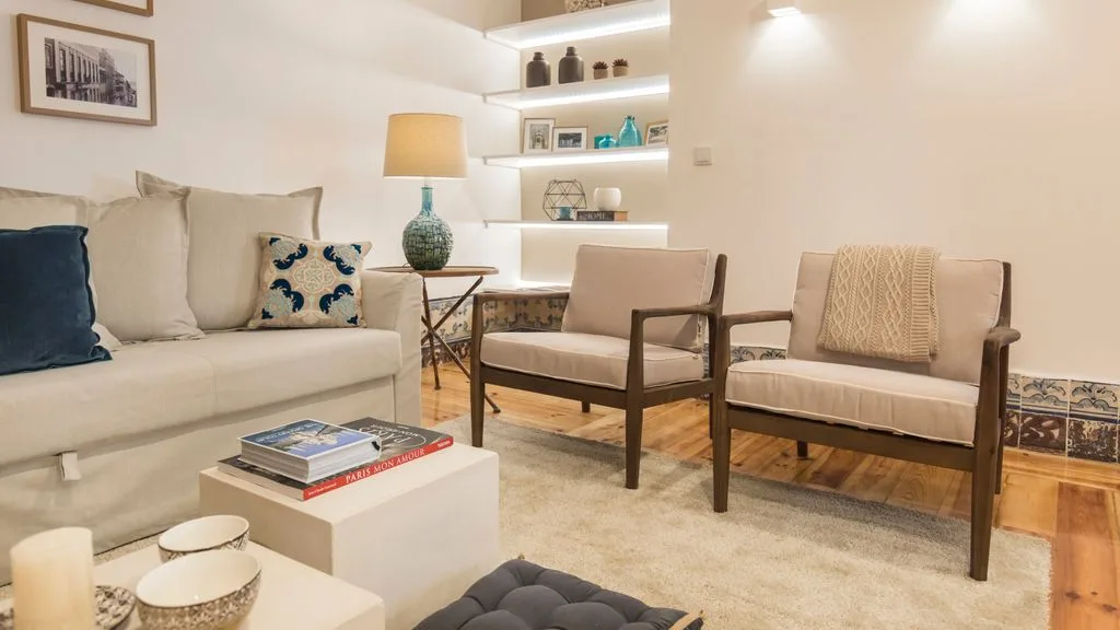 Una sala de estar con un sofá, dos sillones y estantes de pared iluminados.