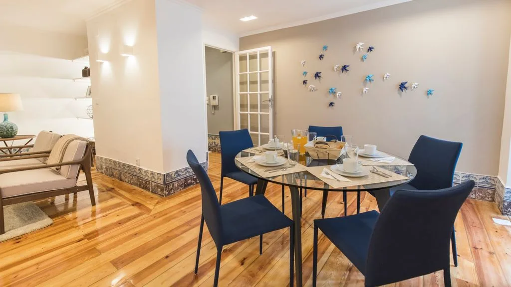 Un comedor con una mesa preparada con vajilla y asientos azul oscuro.