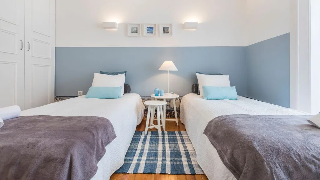 Un dormitorio con dos camas y una alfombra de rayas azules entre ellas.