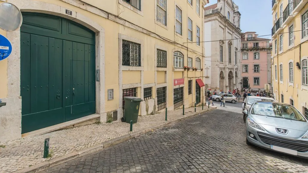 Una calle empedrada discurre entre edificios de tonos pastel con coches aparcados.