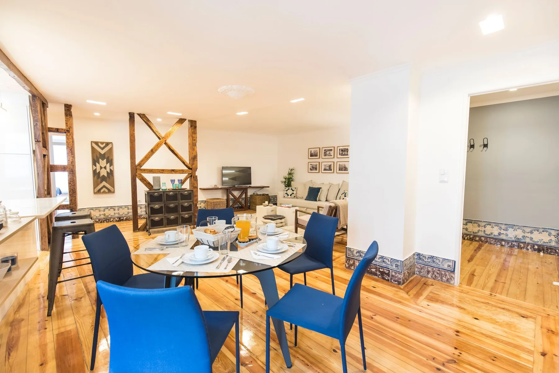 Una zona de comedor y sala con la mesa puesta, asientos azules y un televisor.