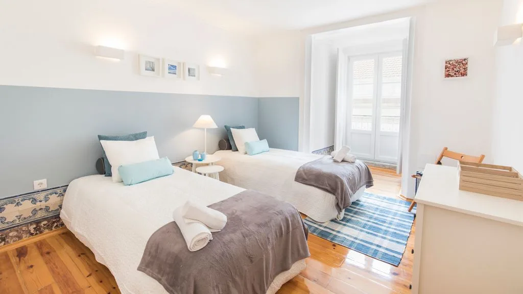 Un dormitorio luminoso con dos camas, una pared azul y una alfombra a rayas.