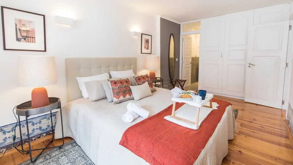 Un dormitorio luminoso con una cama bien arreglada y una colcha roja.