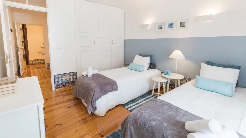 Un dormitorio luminoso con dos camas, armarios blancos y paredes azul claro.