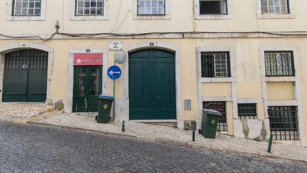 Una calle muestra la entrada y las ventanas de un edificio claro junto a una vía empedrada.