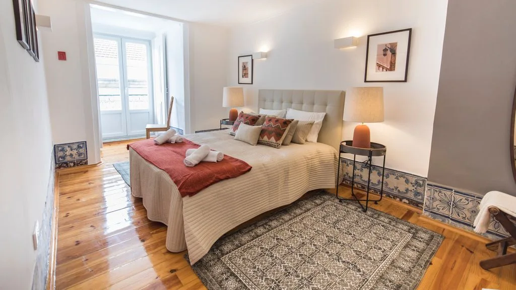 Un dormitorio luminoso con una cama grande, una alfombra estampada y puertas de cristal.