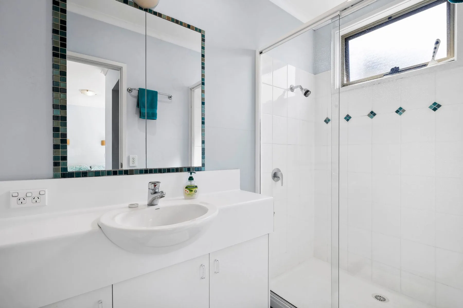 Un baño luminoso con lavabo, espejo y ducha de vidrio.