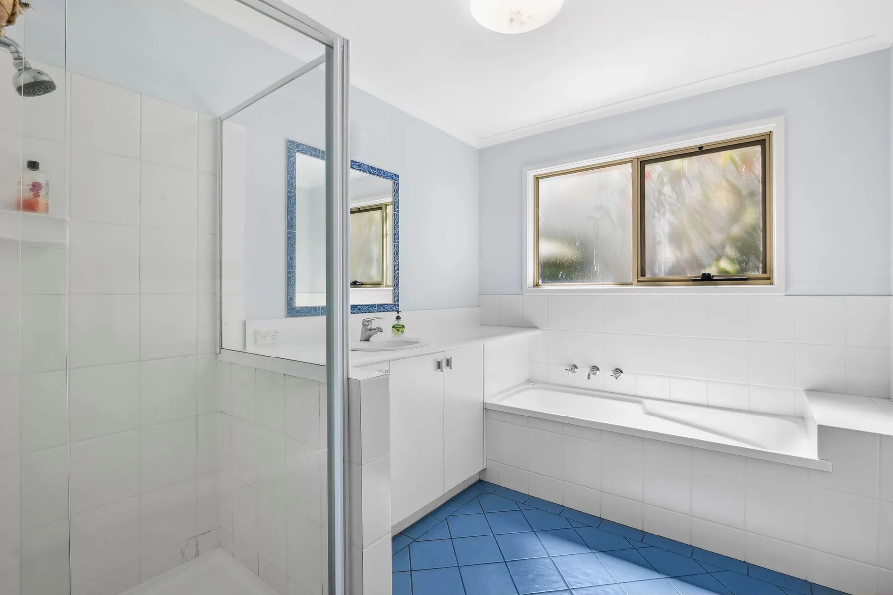Un baño luminoso con una ducha de vidrio y una bañera bajo la ventana.