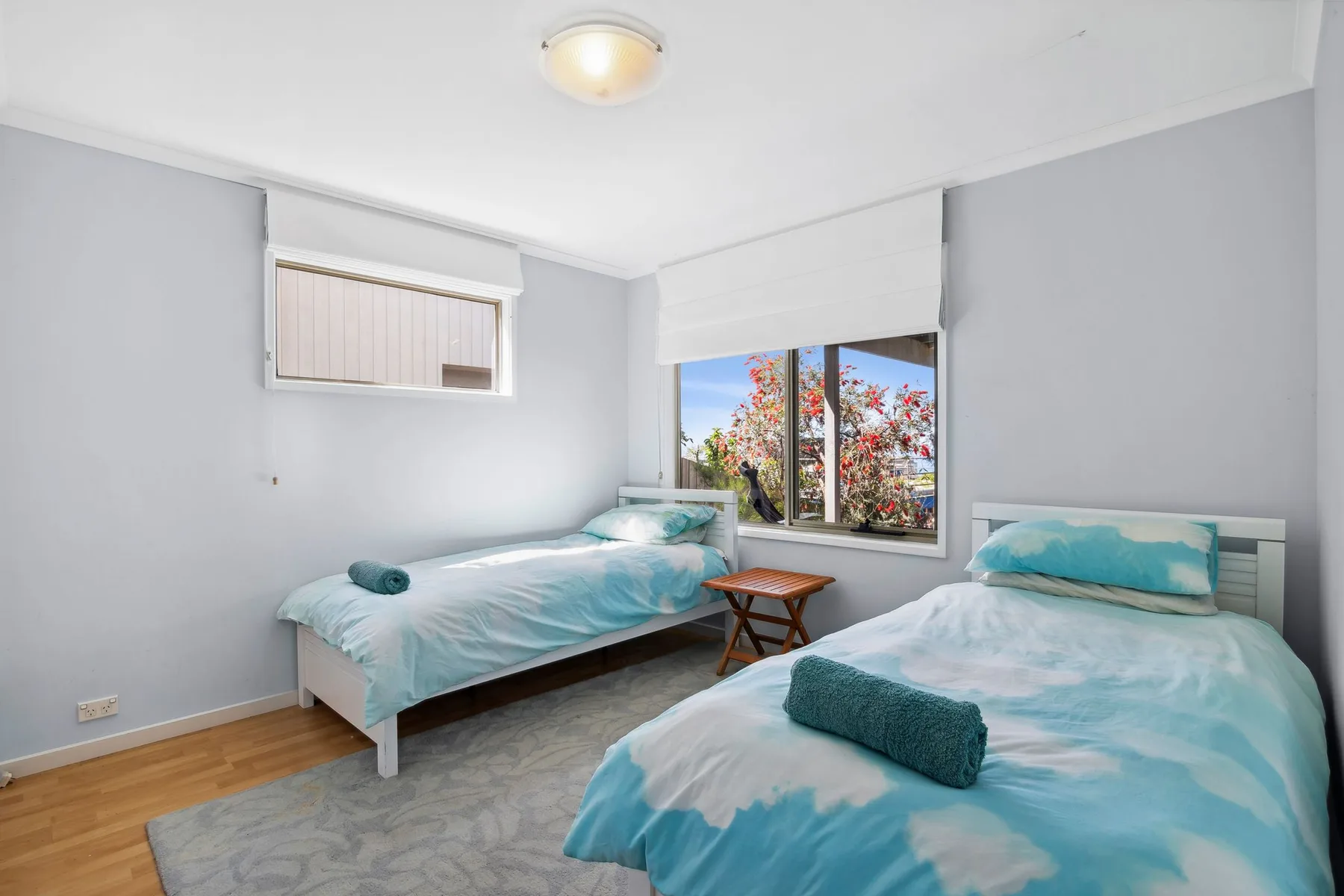 Un dormitorio luminoso con dos camas y una ventana con vistas a los árboles.