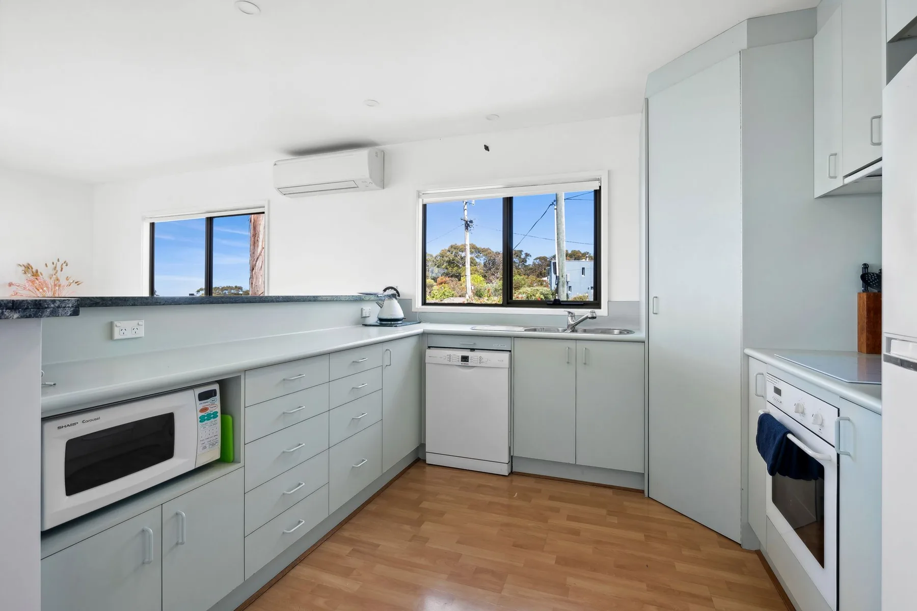 Una cocina luminosa con gabinetes blancos y ventanas con vista a los árboles.