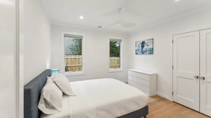 A bright bedroom with a bed, two windows, and a white dresser.
