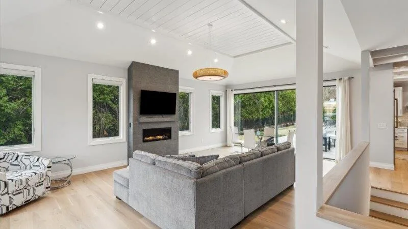 A bright living room with gray seating and large windows overlooking greenery.