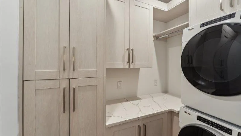 A laundry area with stacked machines, pale cabinets, and a countertop.