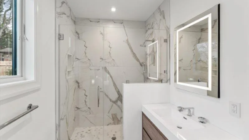 A bright marble-tiled bathroom with a glass shower and a vanity.