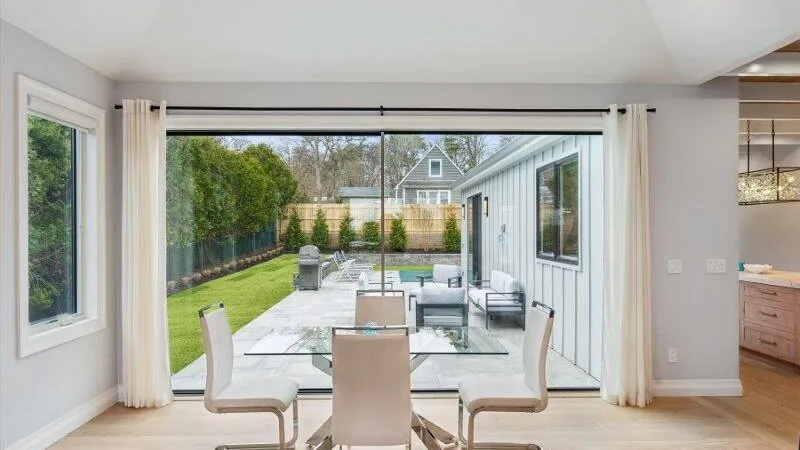 A bright dining area opens onto a patio with outdoor seating and a lawn.