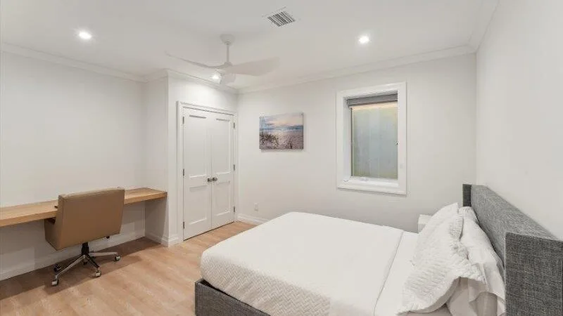 A bright bedroom with a bed, desk, and window.