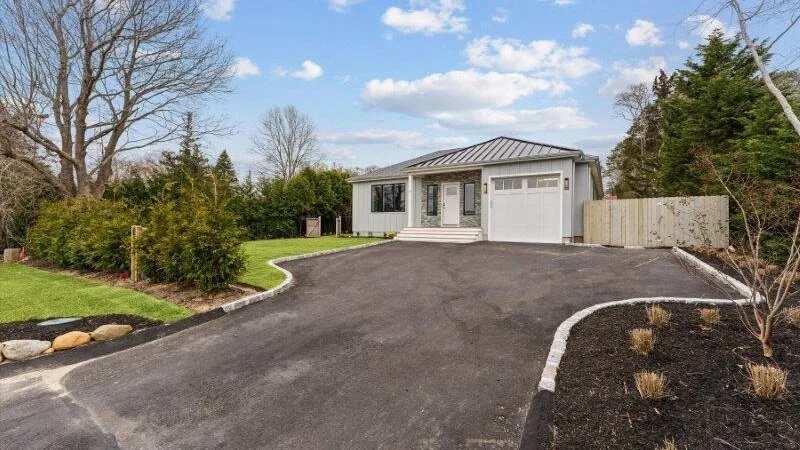 A single-story house sits beside a wide paved driveway and landscaped yard.
