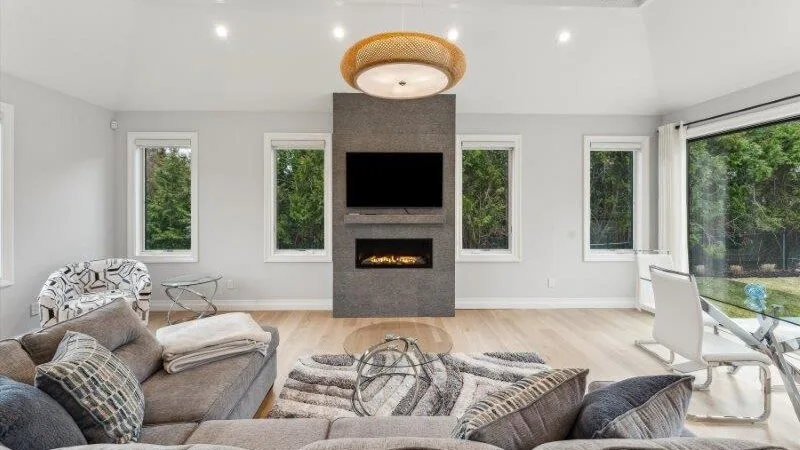 A bright living room with seating, a television, and large windows overlooking greenery.