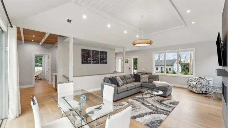 A bright living room with gray seating, a glass coffee table, and large windows.