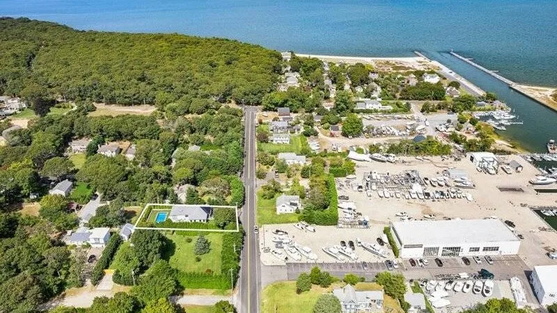 An aerial view of a coastal marina, with boats and a wooded shoreline.