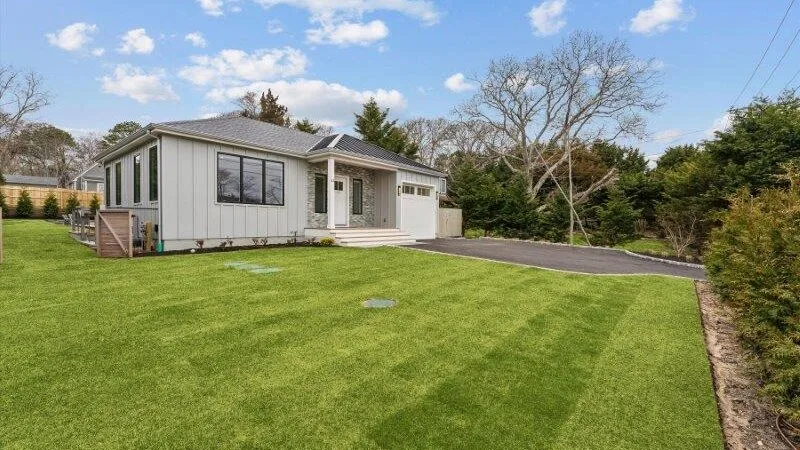 A single-story house with a broad green lawn and a paved driveway.